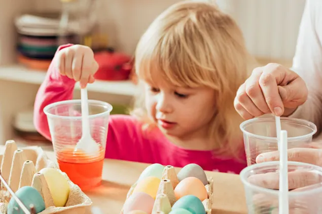 Young child dyeing Easter eggs with an adult